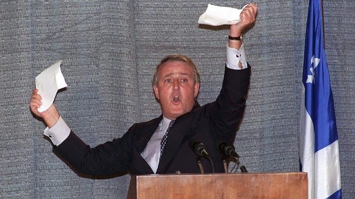 Brian Mulroney déchire un papier sur un podium.