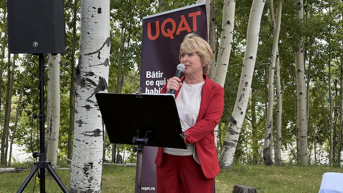 Anick Lavoie parle au micro derrière un lutrin devant une affiche de l'UQAT.