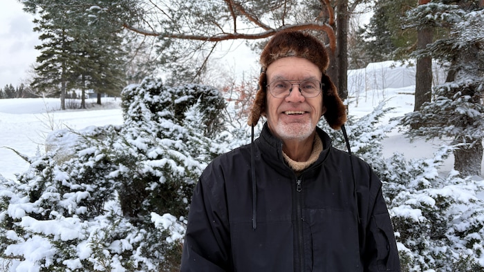 Un homme pose à l'extérieur sous la neige.