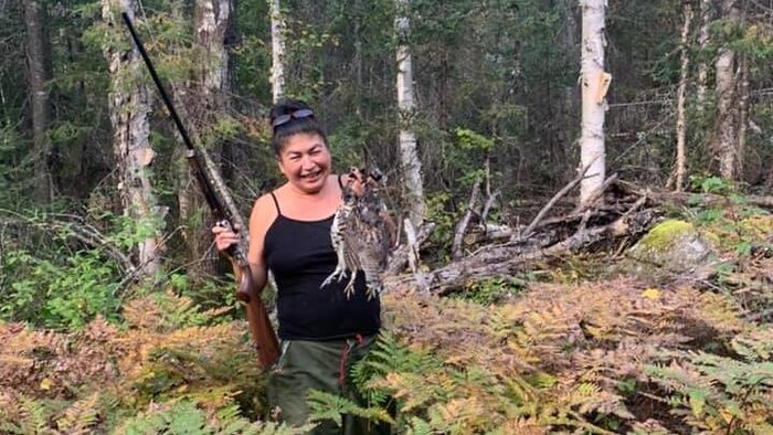 Une femme avec deux perdrix mortes dans une main et un fusil dans l'autre.