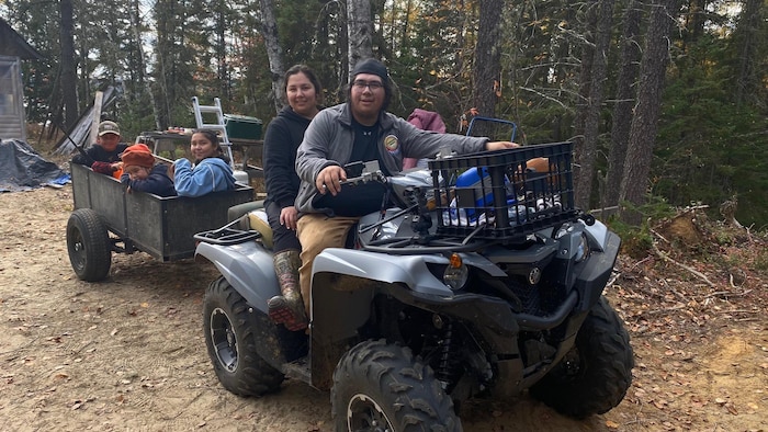 Une homme et une femme sont sur un VTT. À l'arrière est accrochée une cariole contenant 4 enfants.