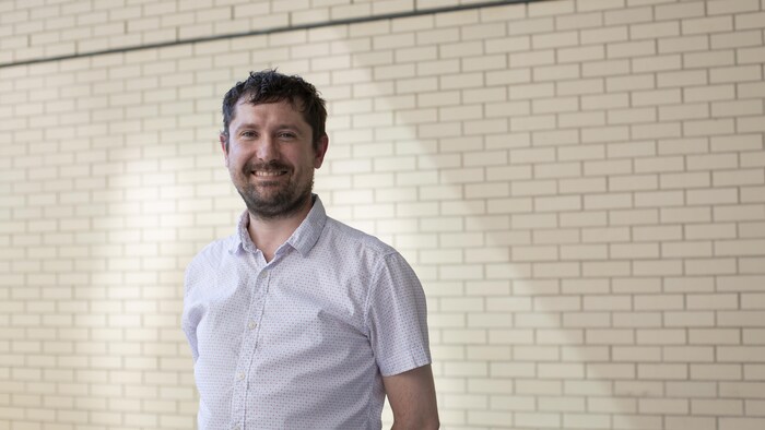 Portrait de Guillaume Dumas qui prend la airs  devant un mur de briques jaunes.