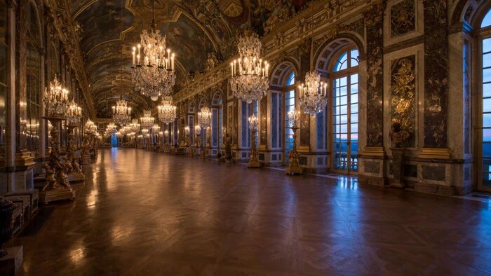 Une salle du château richement décorée et éclairée par des chandeliers.
