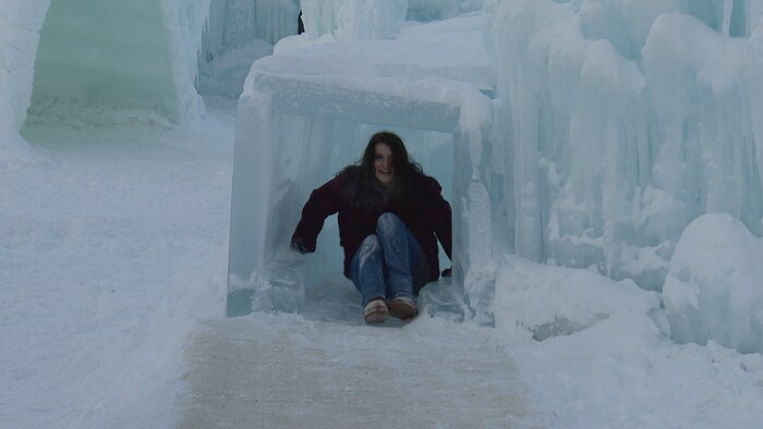 Une jeune femme sourit en sortant d’un petit tunnel de glace sculpté au sein d'un château de glace.