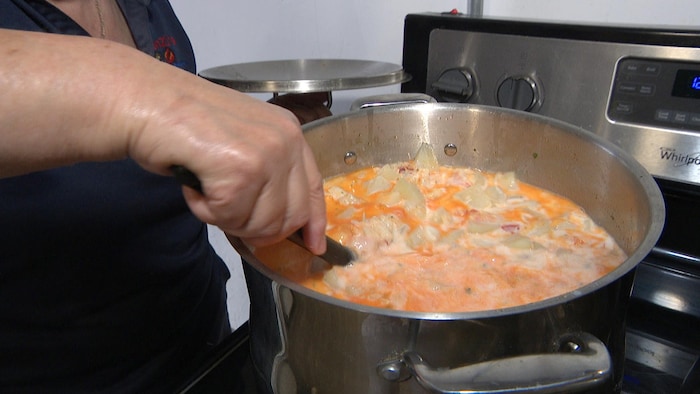Sur une cuisinière Whirlpool, une femme brasse une mixture orange et blanche, agrémentée de gros grumeaux, dans une grosse chaudière.