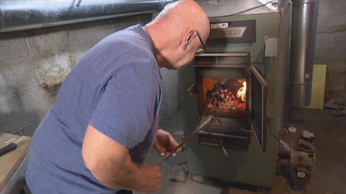 Un homme utilise un tisonnier pour bouger le bois dans son poêle. 