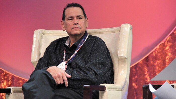 Gilbert Dominique assis dans un fauteuil lors d'un panel de discussion.