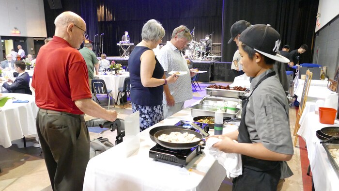 Un cuisinier a une casserole à la main, alors que des gens emplissent leur assiette, au Centre culturel franco-manitobain.