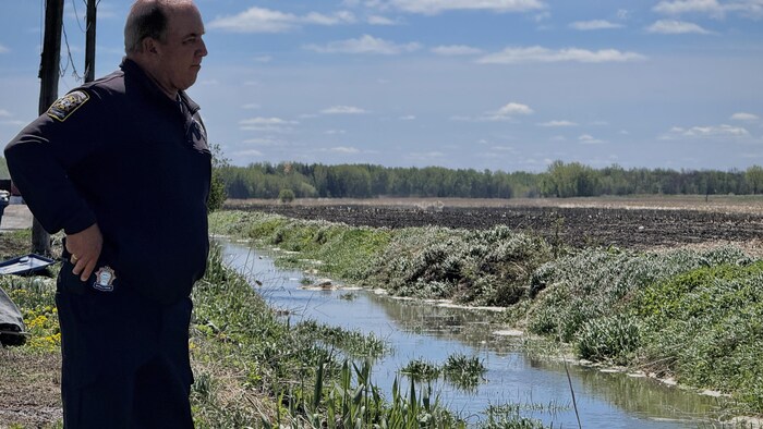 Un pompier regarde le fossé rempli d'eau contaminée, les mains sur les hanches.
