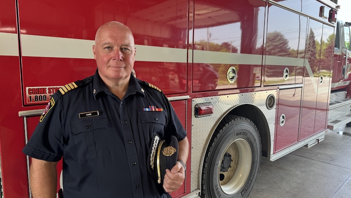 Le chef des pompiers, Chris Case, devant un camion et un chapeau à la main.
