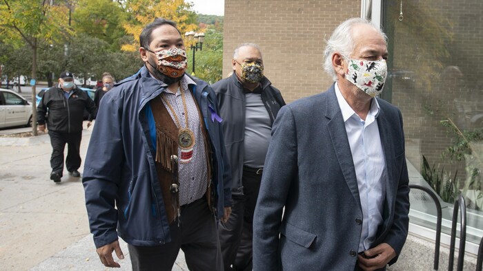 Trois hommes portant des masques marchent dans la même direction.