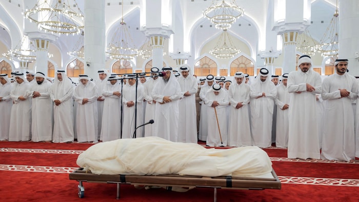 Des hommes vêtus de blanc pour les funérailles se recueillent devant le défunt.