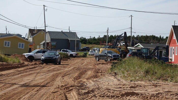 Un chemin de terre travaillé par des machinerie entouré de chalets dont certains ne sont plus au niveau.