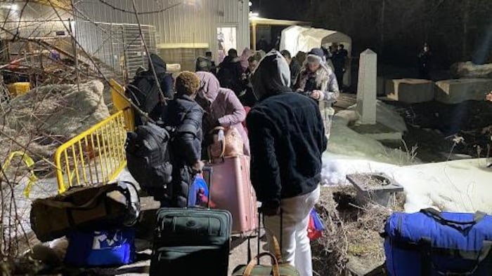 Des demandeurs d'asile font la file devant un petit bâtiment le soir.