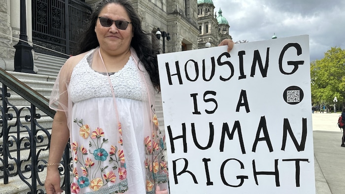 Cheri Jacobs sur les marches de l'Assemblée législative, à Victoria, le 7 mai 2024, avec une pancarte qui affirme que le logement est un droit humain.