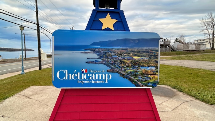 Une petite structure en bois représentant un phare peint aux couleurs de l'Acadie et décoré d'une étoile jaune, avec une affiche soulignant l'entrée de Chéticamp.