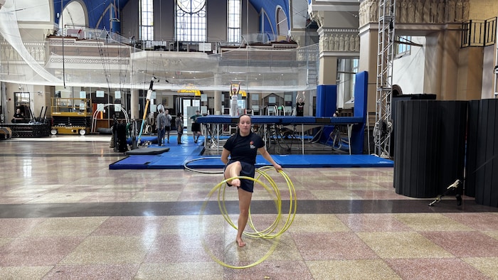 Une circassienne manipule plusieurs cerceaux au centre d'un vaste gymnase aménagé pour les arts de la scène.