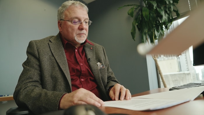 Portrait de Daniel Jean, assis à un bureau devant des papiers.