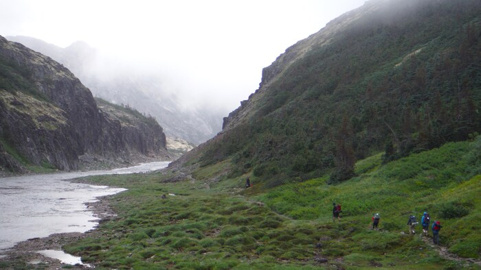 Des gens marchent sur un sentir près d'une rivière et des montagnes. 