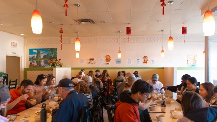 Des dizaines de personnes mangent à table dans un restaurant.