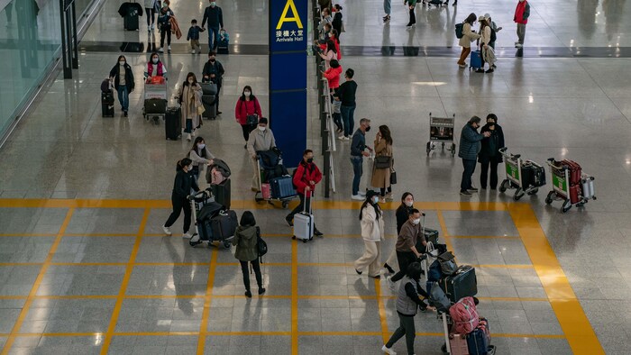 Des gens marchent avec leurs bagages dans le hall d'arrivée de l'aéroport international de Hong Kong.