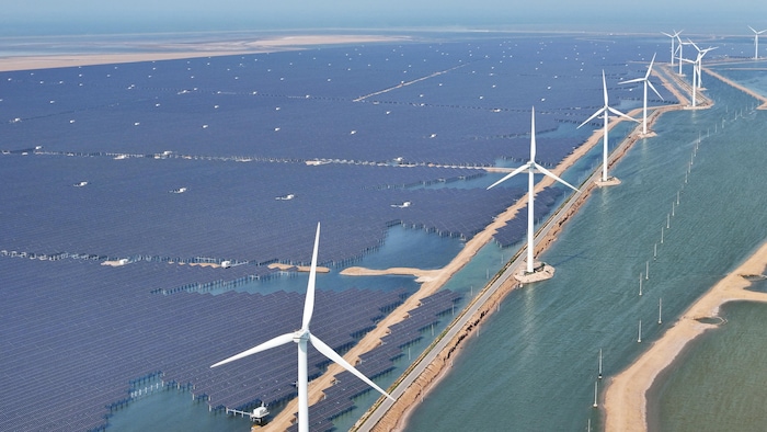 Des milliers de panneaux solaires sont aménagés sur un plan d'eau. Une dizaine d'éoliennes les surplombent.