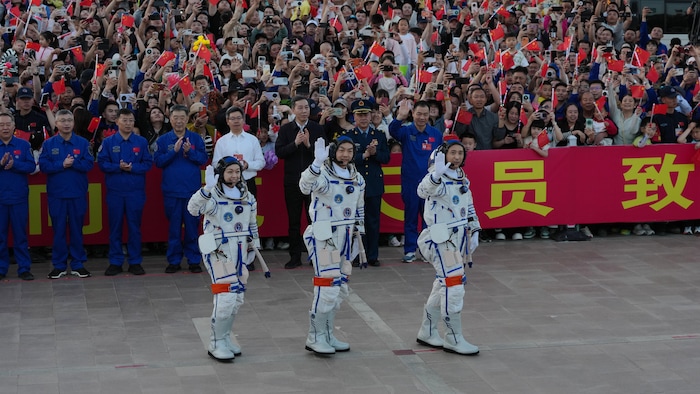 Trois personnes saluent la foule qui agite des drapeaux aux couleurs de la Chine.