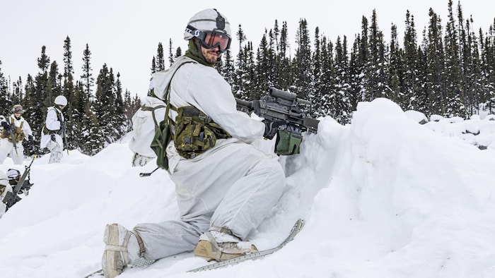Un soldat, vêtu de blanc, porte des raquettes et des lunettes de ski.