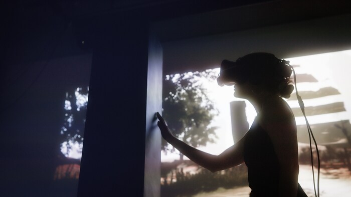 Une personne munie d'un casque de réalité virtuelle touche de la main une colonne noire. 