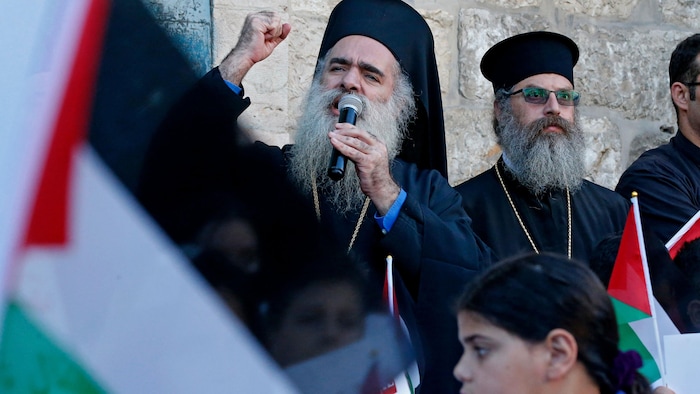 Un homme religieux chrétien qui porte une longue barbe grisâtre gesticule d'une main en tenant un micro de l'autre.