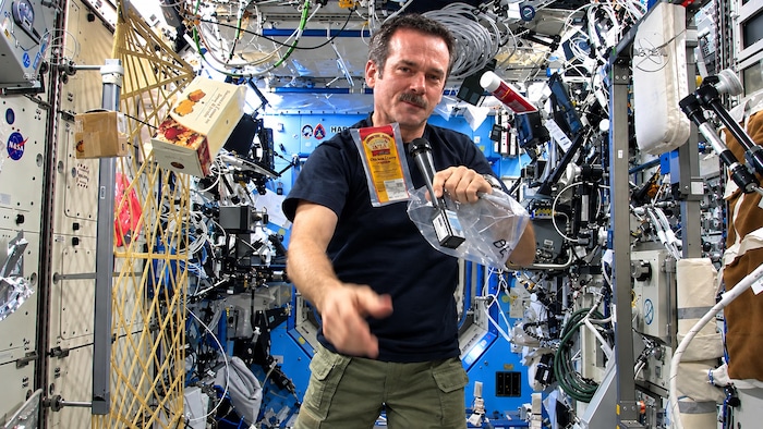 Chris Hadfield flotte dans la station spatiale internationale. Il montre à la caméra un batônnet de viande séchée de bison.