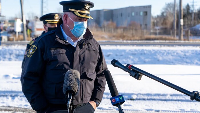 Un homme portant un masque en conférence de presse dehors, face à des micros.