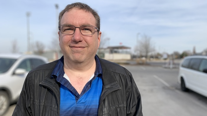 Chris Mallon porte un manteau et des lunettes