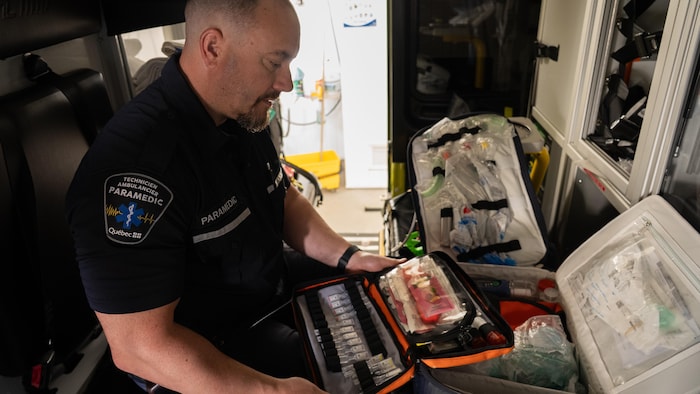Un ambulancier en uniforme assis dans une ambulance avec un sac ouvert de fioles de médicaments.