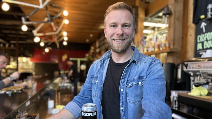 Christian Gouin se tient fièrement derrière le bar avec une bière qui porte le nom Éclipse. 