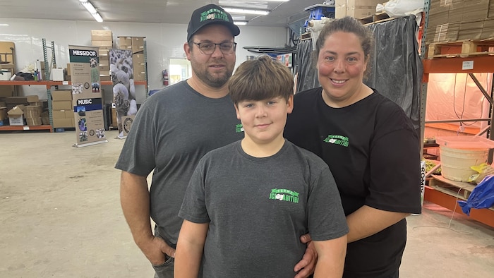 Un couple et son fils sourient à la caméra en posant à l'intérieur d'un bâtiment de ferme.
