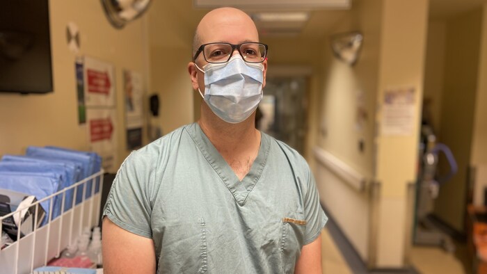 الدكتور كريستيان مالو، بقناع وجه، يقف في المستشفى وينظر إلى عدسة المصور.