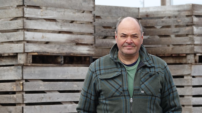 Une photo de Christian Poirier, devant des installations de bois, à l'extérieur.