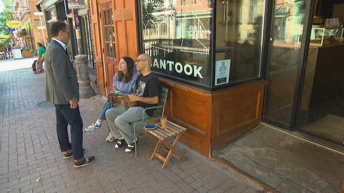 Un homme parle à des gens assis sur une chaise à l'extérieur d'un café.