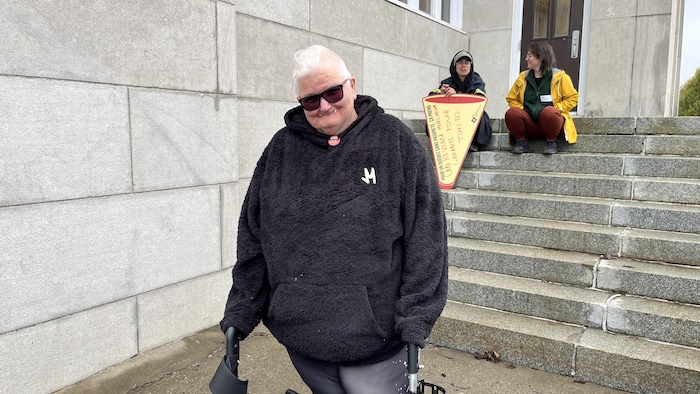 Une dame âgée avec sa marchette pose sur le parvis de l'église à Saint-Robert, dans Rimouski.
