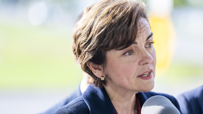 Christine Fréchette, les cheveux courts bruns et vêtue d'une veste foncée, s'exprime devant un micro.