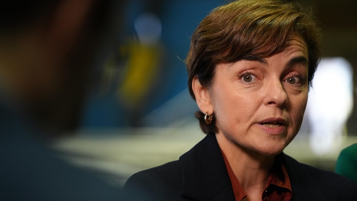 Gros plan sur Christine Fréchette qui s'exprime devant des microphones, vêtue d'une veste sombre.