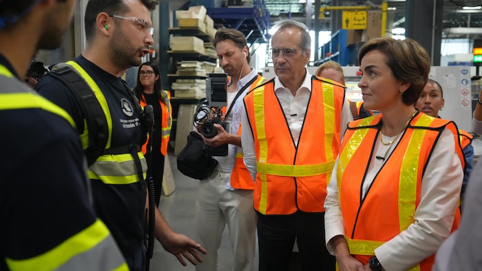 Christine Fréchette visite l'usine avec Richard Voyer, les deux portent des vestes réfléchissantes.