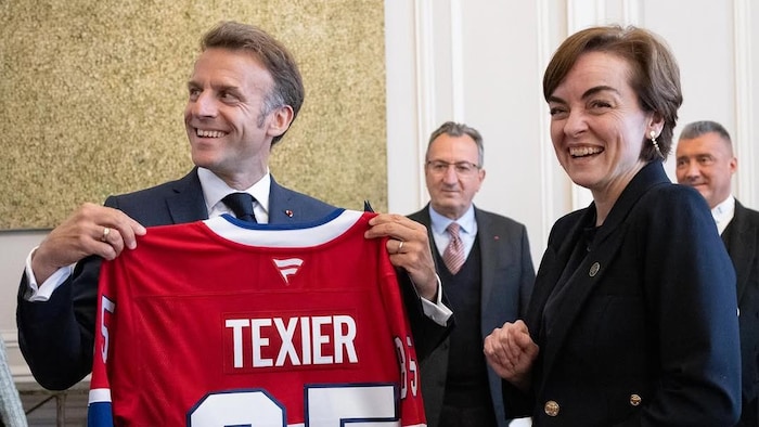 Emmanuel Macron tient un un chandail d'Alexandre Texier, debout aux côtés de Christine Fréchette.