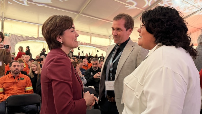 Les trois élus discutent dans une salle pleine de gens assis.