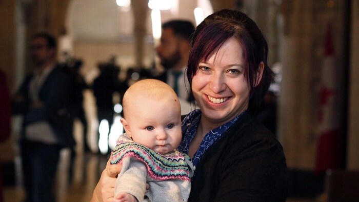 Christine Moore avec sa fille bébé dans ses bras dans un corridor du parlement à Ottawa.