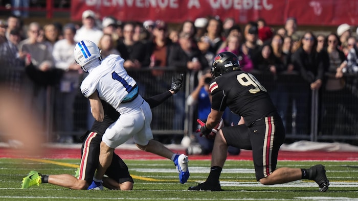 Un joueur des Carabins devant lui, un joueur du Rouge et Or attrape le ballon dans les airs, un genou au sol.