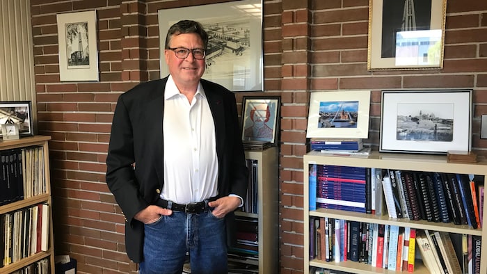 Un homme se tient les mains dans les poches, à côté d'une bibliothèque remplie de livres.
