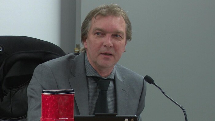 Vêtu d'un veston gris, le conseiller Christopher Fisher prend la parole lors d'une réunion du conseil municipal de Nipissing Ouest. 