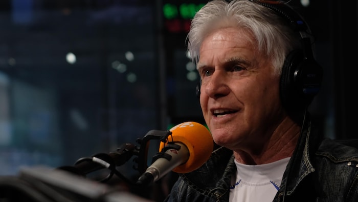 Le chroniqueur Marcel Bouchard derrière un micro en entrevue dans un studio de radio.